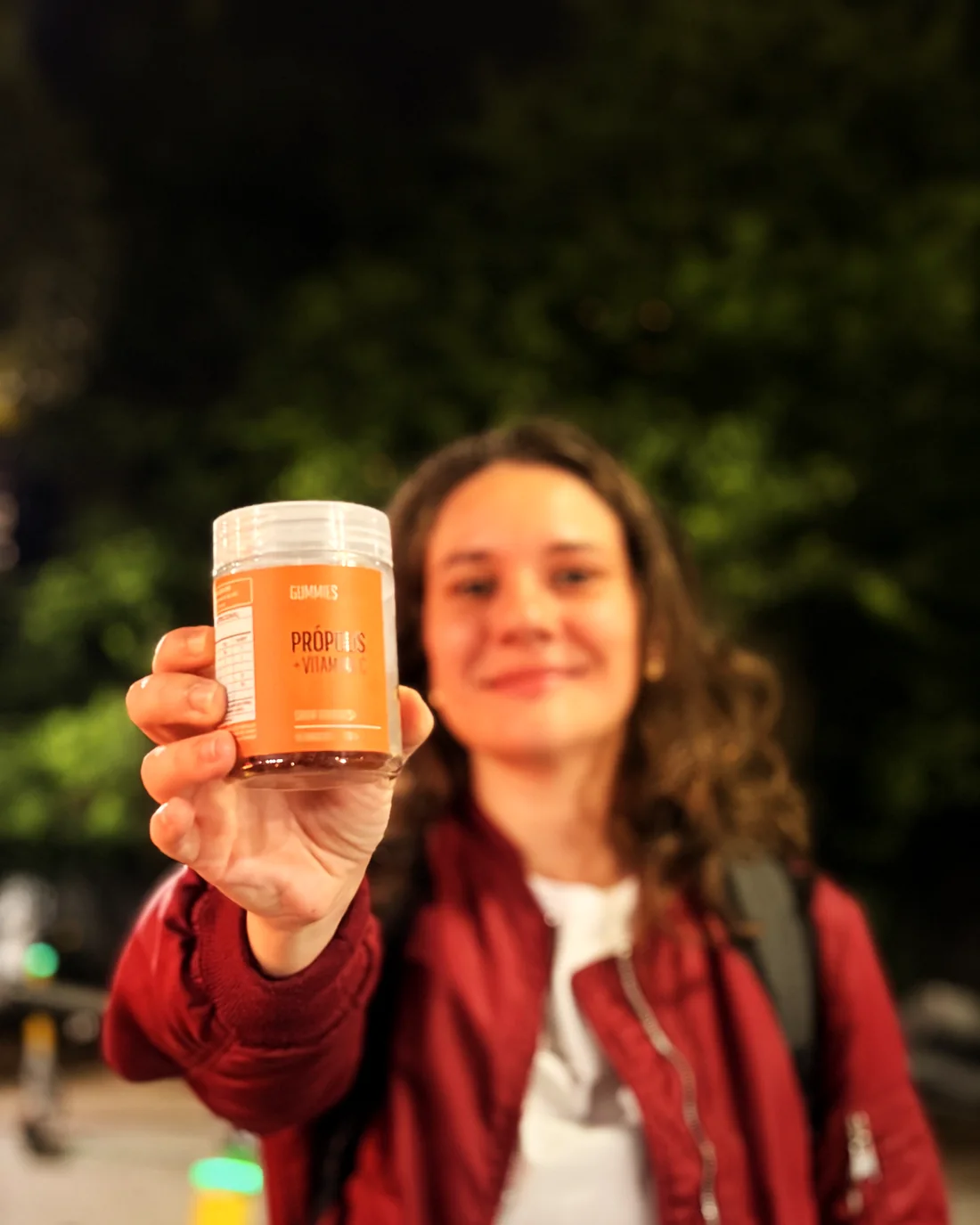 Mulher sorrindo e mostrando o pote da goma de própolis GoCore (foto real)