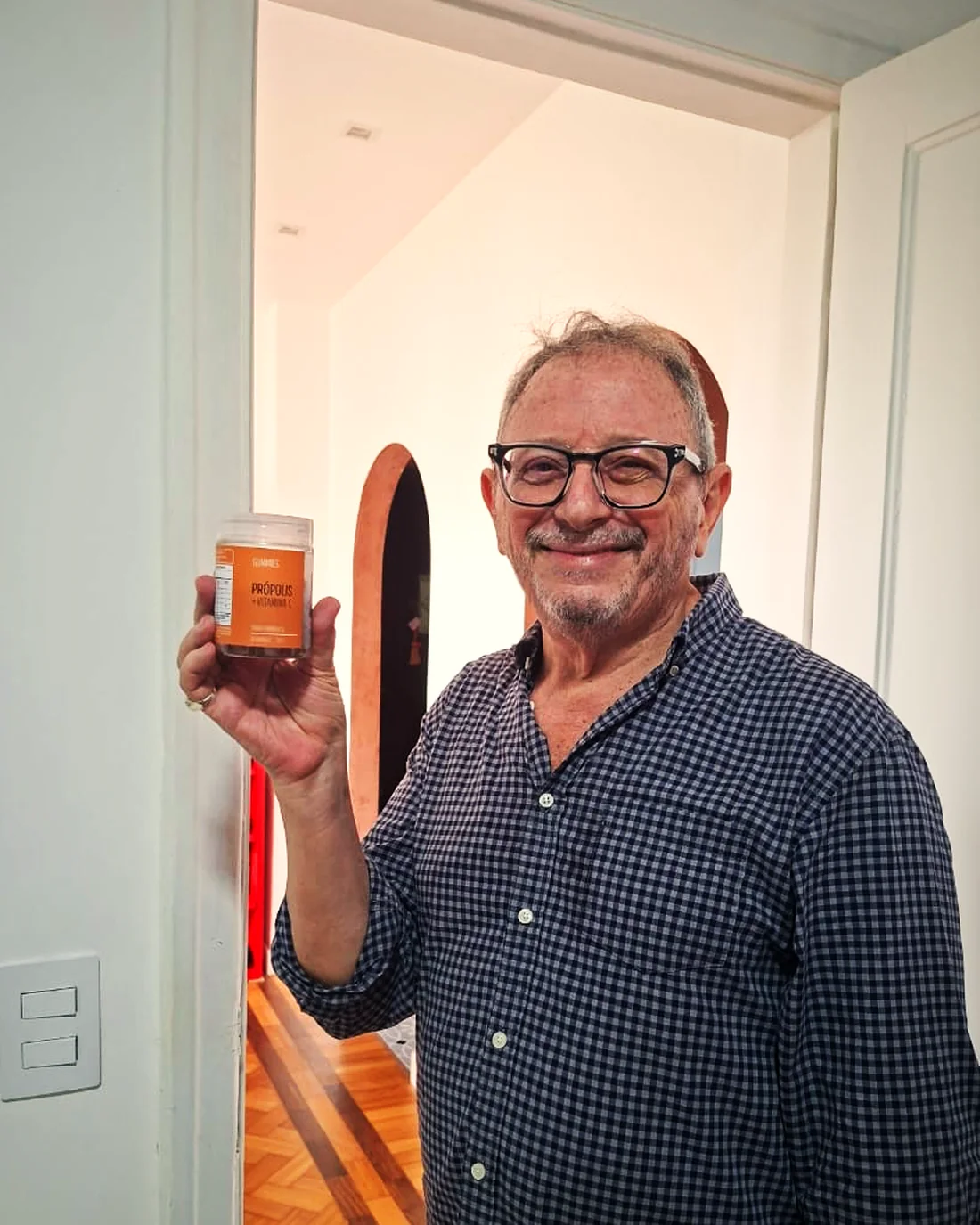 Homem de óculos sorrindo e mostrando o pote da goma de própolis GoCore (foto real)